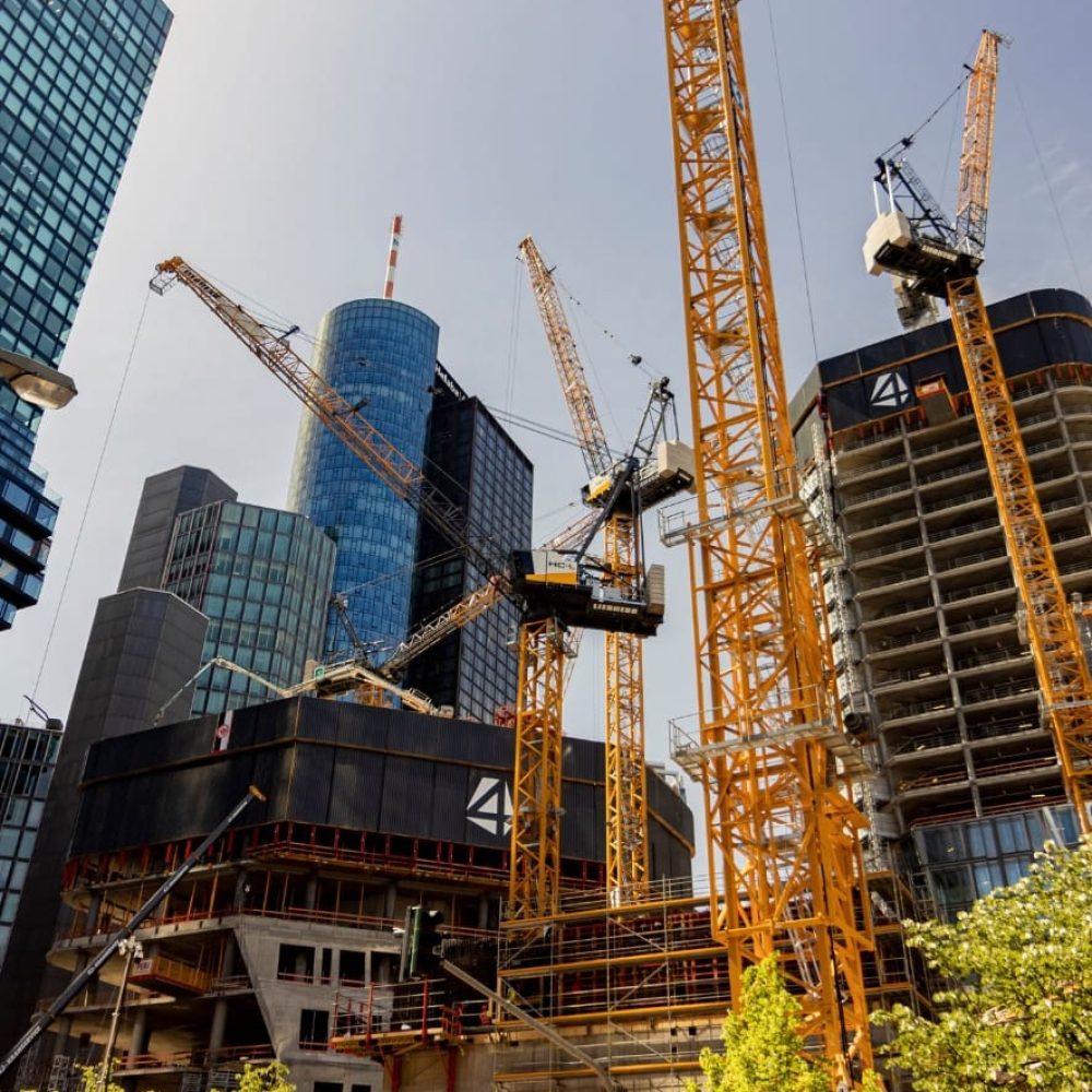 Multiple tower cranes operating on a high-rise construction site in an urban city centre.