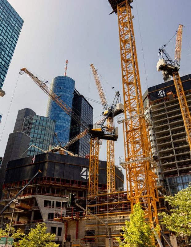 Multiple tower cranes operating on a high-rise construction site in an urban city centre.